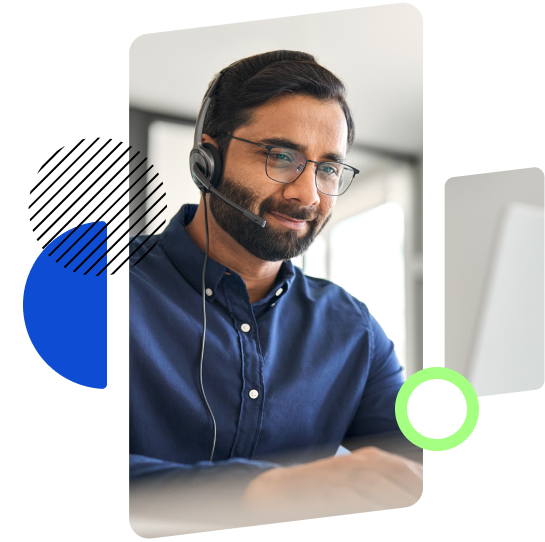 A man wearing glasses and a headset, smiling while working at a computer, likely engaged in a virtual meeting or support session.